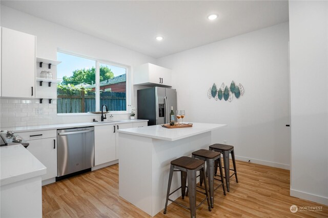 kitchen featuring stainless steel appliances, white cabinets, sink, decorative backsplash, and light wood-type flooring