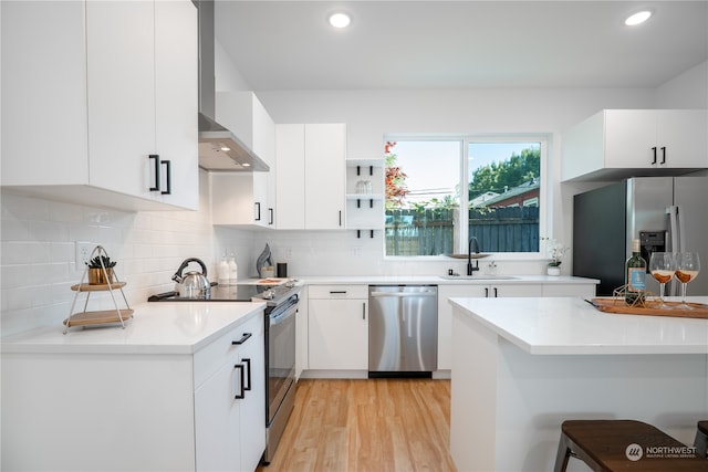 kitchen with a breakfast bar area, light hardwood / wood-style flooring, wall chimney range hood, stainless steel appliances, and sink