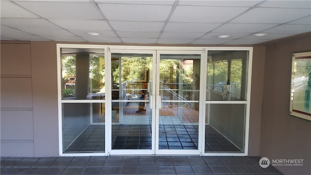 doorway to outside with dark tile patterned flooring and a drop ceiling