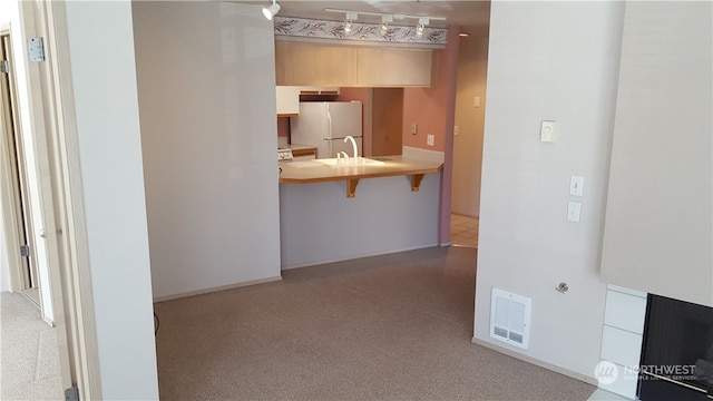 interior space with white refrigerator, a breakfast bar, sink, light brown cabinets, and light carpet