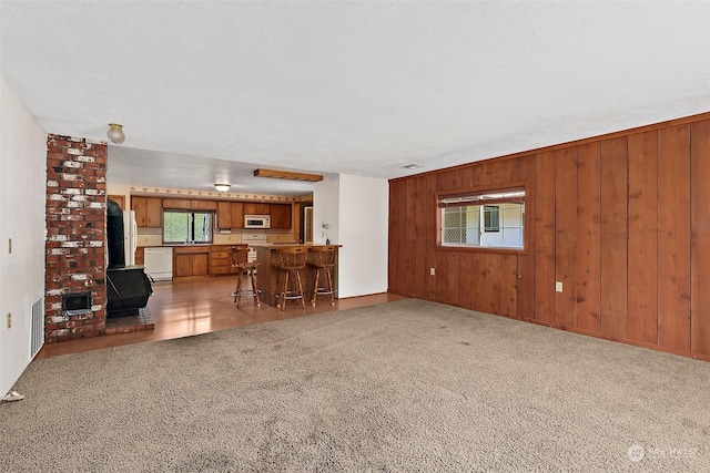 unfurnished living room featuring wood walls, indoor bar, carpet floors, a wood stove, and a textured ceiling