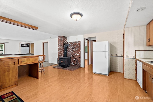 kitchen featuring a wood stove, a textured ceiling, white appliances, and light hardwood / wood-style floors