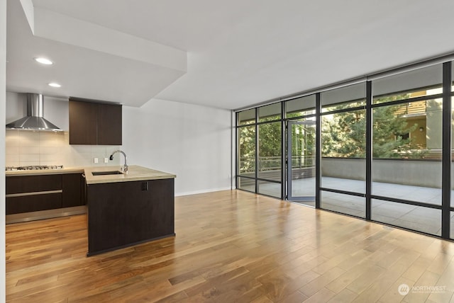 kitchen featuring sink, light hardwood / wood-style flooring, a wall of windows, decorative backsplash, and wall chimney range hood