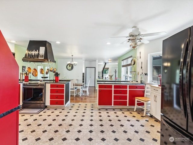 kitchen with black refrigerator, exhaust hood, ceiling fan with notable chandelier, and stainless steel range with electric stovetop