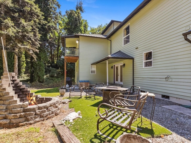 back of house featuring a balcony, a lawn, and a fire pit