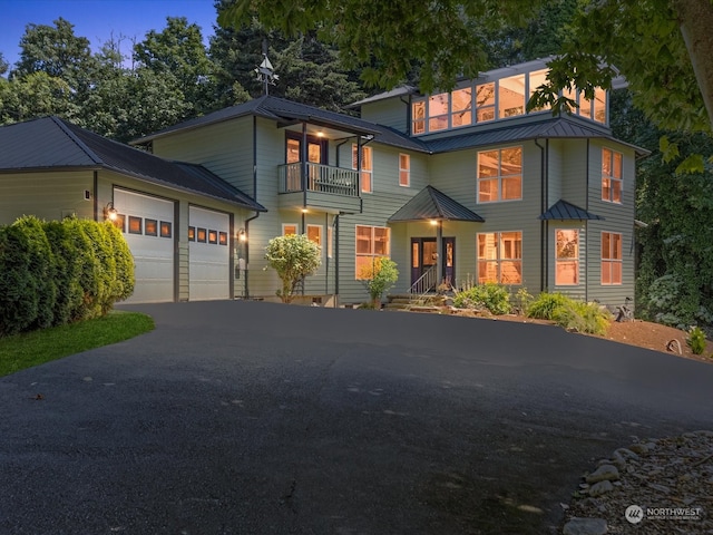 view of front of property featuring a garage, a balcony, a standing seam roof, driveway, and metal roof