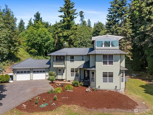 view of front facade with an attached garage, aphalt driveway, a balcony, a standing seam roof, and metal roof