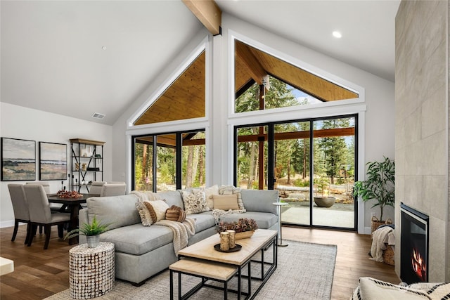 living room featuring beamed ceiling, visible vents, wood finished floors, a tiled fireplace, and high vaulted ceiling