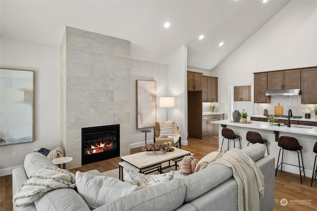 living room featuring recessed lighting, a tile fireplace, light wood-style floors, and high vaulted ceiling