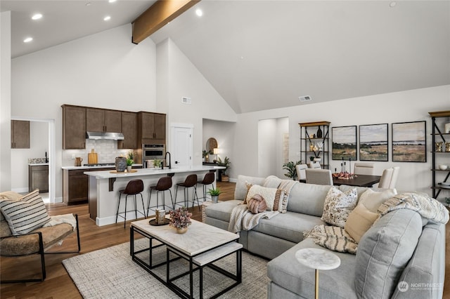 living room with visible vents, high vaulted ceiling, wood finished floors, and beam ceiling