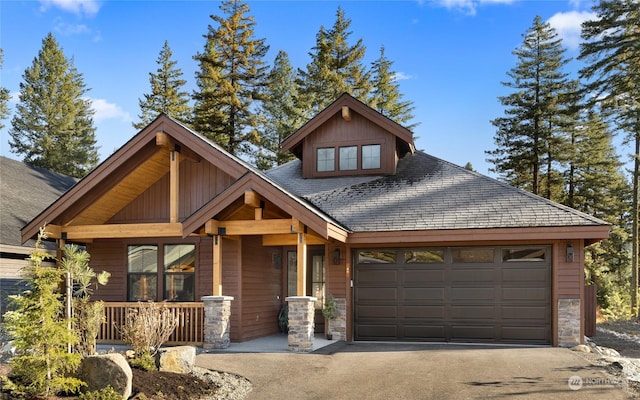 craftsman-style home featuring a porch, a garage, aphalt driveway, and stone siding
