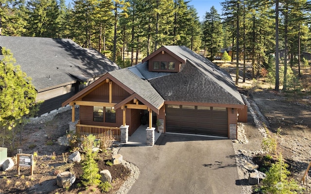 chalet / cabin with driveway, a shingled roof, covered porch, and a garage