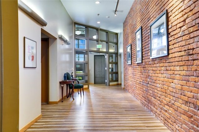 corridor featuring brick wall, hardwood / wood-style flooring, and a towering ceiling