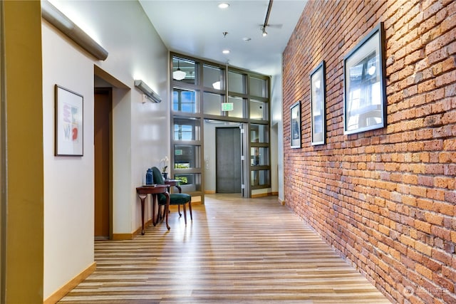 corridor with wood finished floors, baseboards, brick wall, a high ceiling, and an accent wall