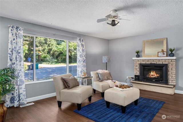 living area with a brick fireplace, a textured ceiling, ceiling fan, and dark hardwood / wood-style flooring