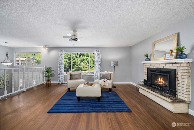 living room featuring ceiling fan, a textured ceiling, dark hardwood / wood-style flooring, and a fireplace