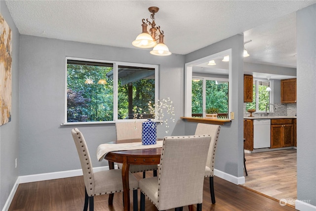 dining area featuring light wood-type flooring, baseboards, a chandelier, and a textured ceiling