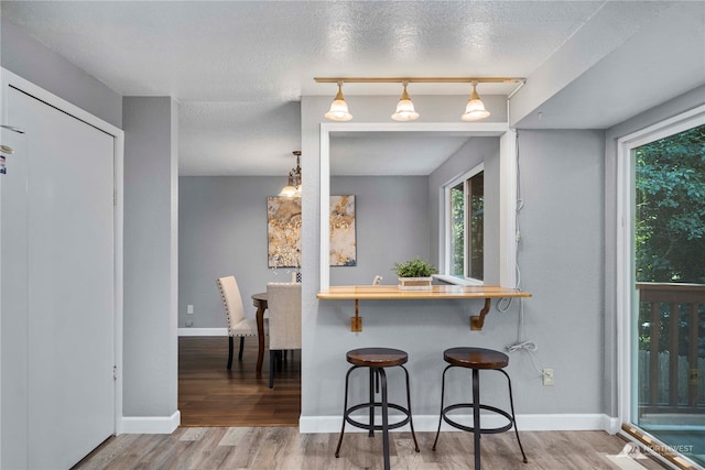 kitchen featuring rail lighting, a breakfast bar, a textured ceiling, wood-type flooring, and decorative light fixtures