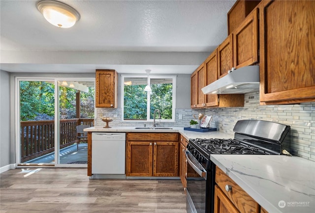 kitchen featuring white dishwasher, under cabinet range hood, a sink, stainless steel gas range, and brown cabinetry