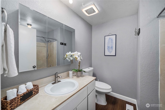 bathroom featuring toilet, wood-type flooring, vanity, a textured ceiling, and walk in shower