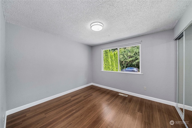 unfurnished room with dark wood-style floors, visible vents, a textured ceiling, and baseboards