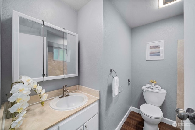 bathroom featuring a textured wall, toilet, vanity, wood finished floors, and baseboards