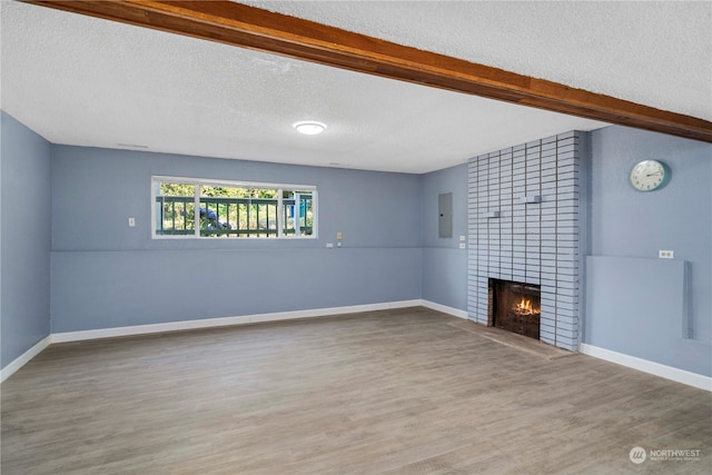 unfurnished living room with beam ceiling, hardwood / wood-style floors, electric panel, a fireplace, and a textured ceiling