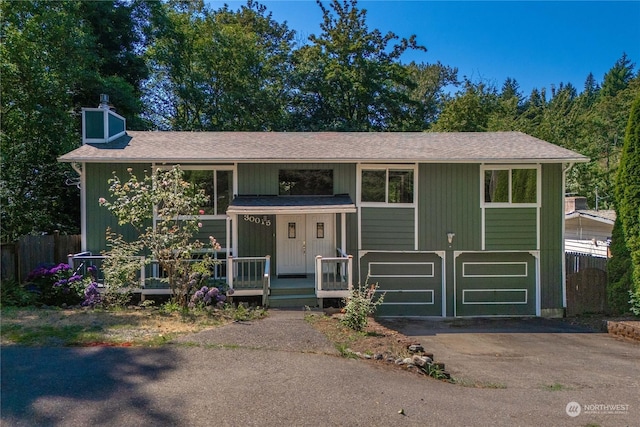 raised ranch featuring a chimney, covered porch, an attached garage, fence, and driveway