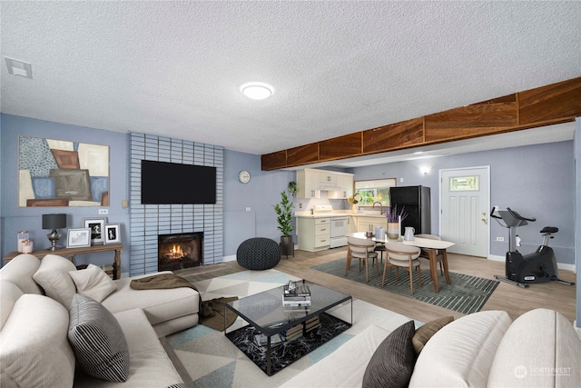 living room featuring sink, a textured ceiling, light hardwood / wood-style flooring, and a fireplace