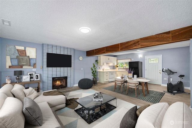 living room with baseboards, visible vents, a textured ceiling, light wood-type flooring, and a brick fireplace