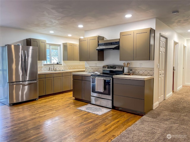 kitchen featuring appliances with stainless steel finishes, light hardwood / wood-style floors, ventilation hood, sink, and gray cabinets