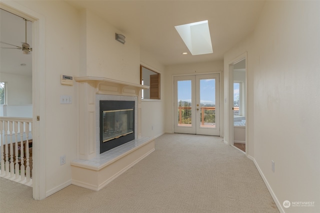 unfurnished living room with ceiling fan, a skylight, french doors, and light colored carpet