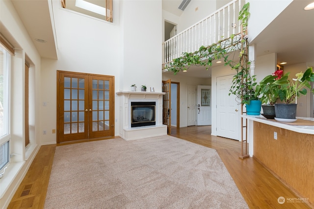 unfurnished living room featuring a healthy amount of sunlight, light wood-type flooring, french doors, and a high ceiling