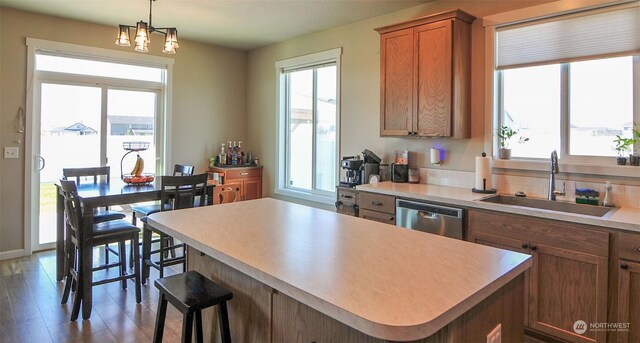 kitchen with dishwasher, light countertops, brown cabinets, hanging light fixtures, and a sink