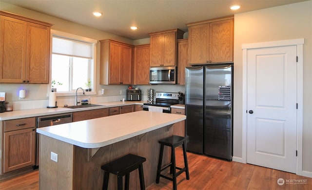 kitchen featuring wood finished floors, recessed lighting, a sink, stainless steel appliances, and a kitchen bar