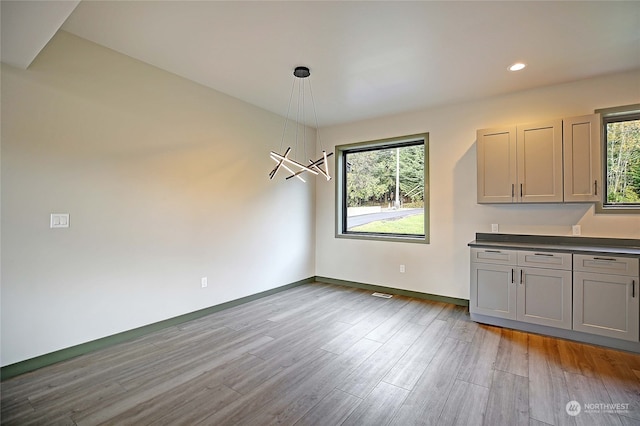 unfurnished dining area with an inviting chandelier, a healthy amount of sunlight, and light hardwood / wood-style floors