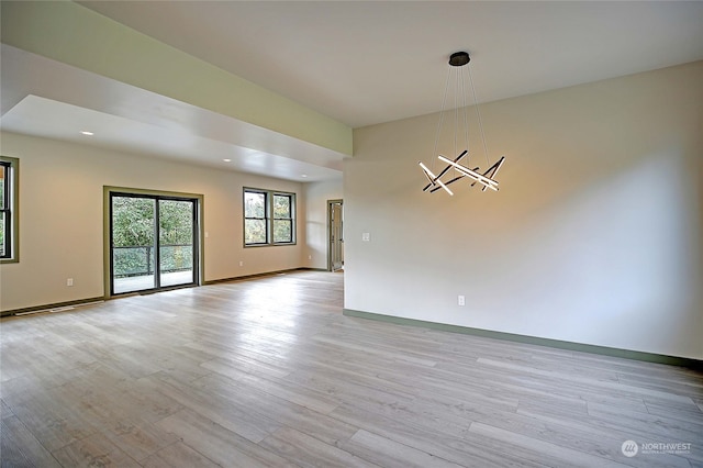 unfurnished room featuring an inviting chandelier and light wood-type flooring