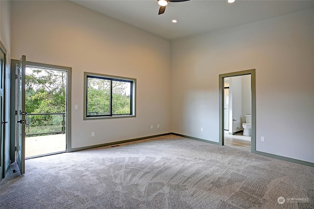 carpeted spare room featuring a towering ceiling and ceiling fan