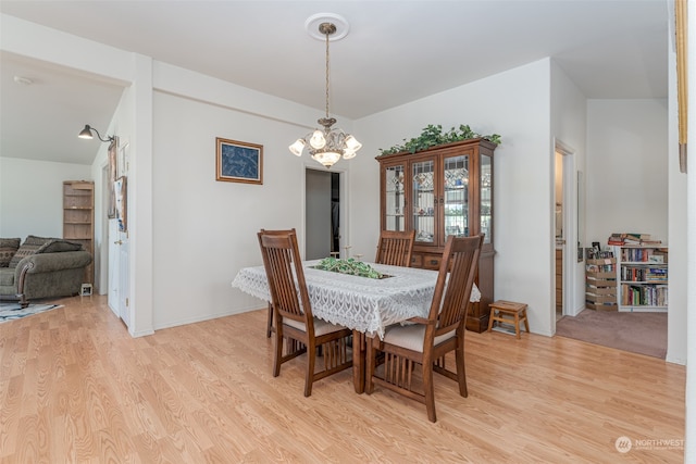 dining room featuring light wood-type flooring, vaulted ceiling, and an inviting chandelier