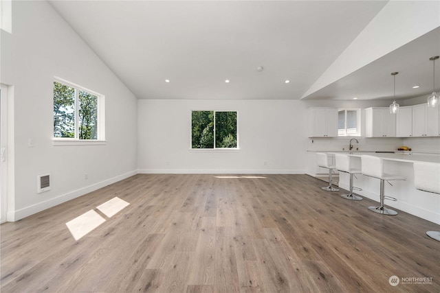 unfurnished living room featuring lofted ceiling, sink, and light hardwood / wood-style floors