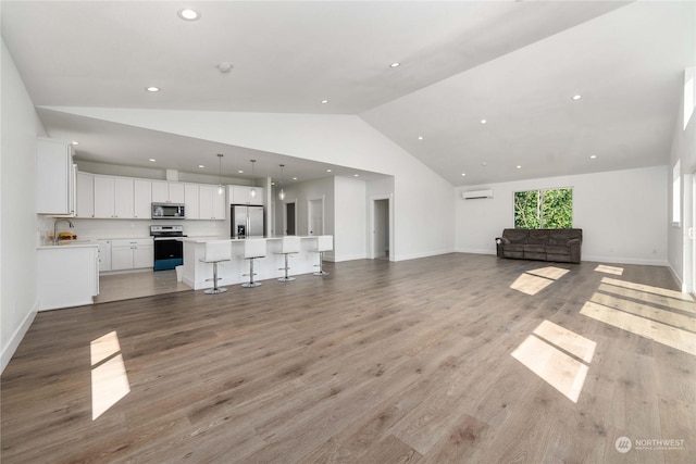 unfurnished living room with sink, a wall mounted AC, lofted ceiling, and light hardwood / wood-style flooring