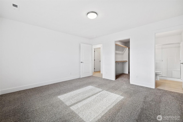 unfurnished bedroom featuring carpet, baseboards, a walk in closet, and a closet