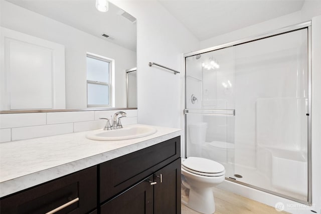 bathroom featuring toilet, wood finished floors, visible vents, vanity, and a stall shower