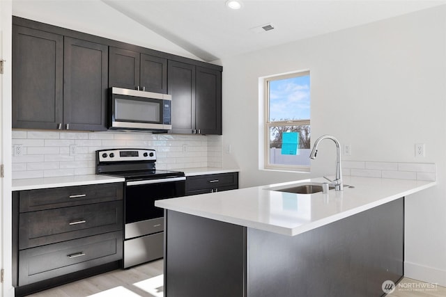 kitchen with visible vents, a sink, vaulted ceiling, stainless steel appliances, and backsplash