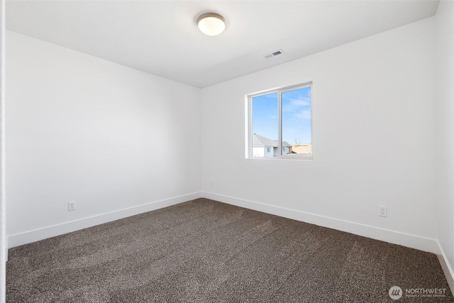 spare room featuring dark carpet, visible vents, and baseboards