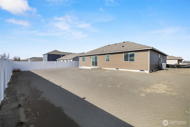 back of property with dirt driveway, central AC unit, a shingled roof, and a fenced backyard