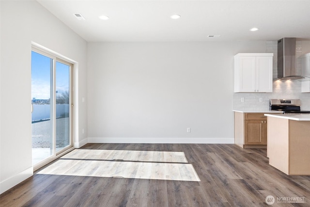 kitchen featuring wall chimney exhaust hood, stainless steel electric stove, decorative backsplash, wood finished floors, and baseboards