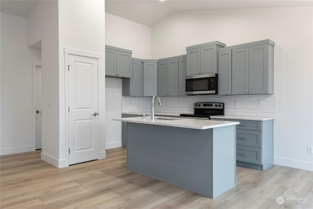 kitchen featuring sink, stainless steel appliances, high vaulted ceiling, decorative backsplash, and a center island with sink