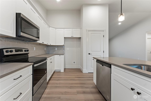 kitchen featuring tasteful backsplash, light hardwood / wood-style floors, pendant lighting, white cabinets, and appliances with stainless steel finishes