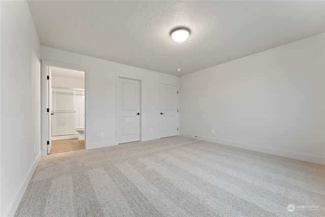 unfurnished bedroom featuring light carpet, a textured ceiling, and ensuite bath